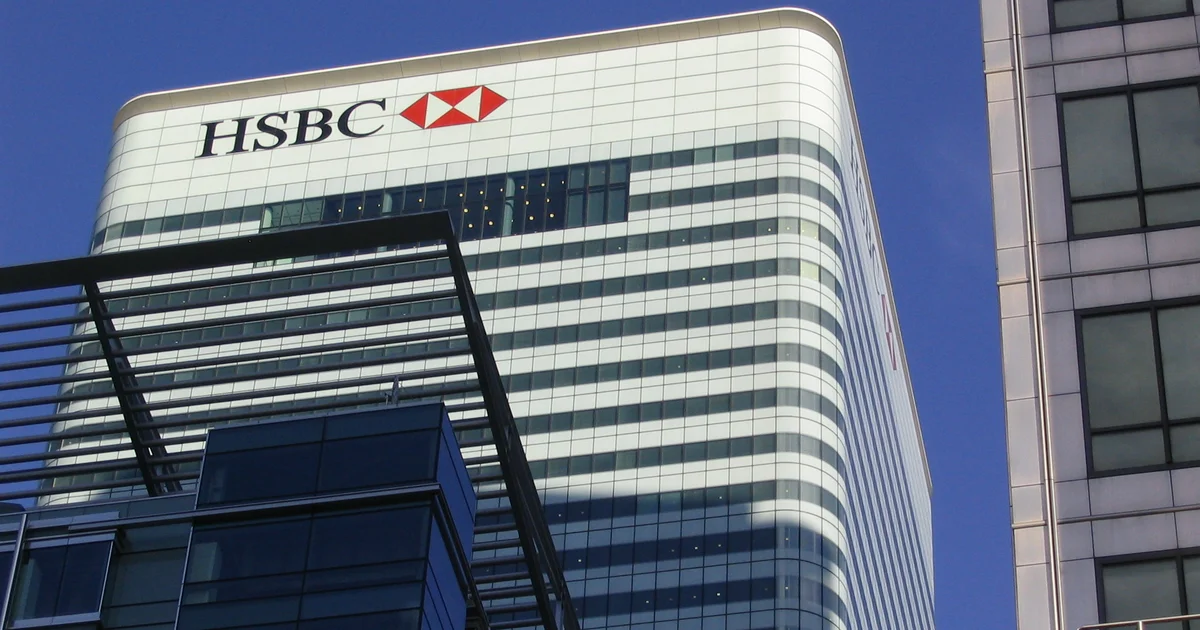 The HSBC tower at Canary Wharf, London, seen from below, its logo on the upper floors against a clear blue sky.