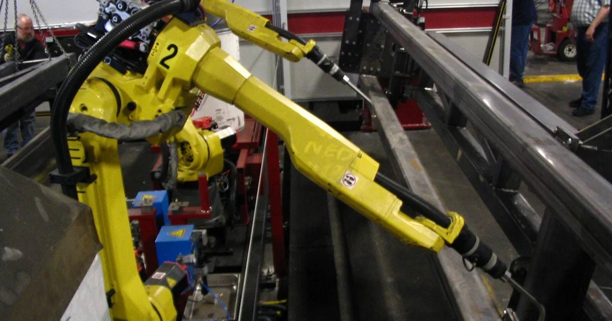 Two industrial robotic arms positioned over a workpiece on a factory production line.