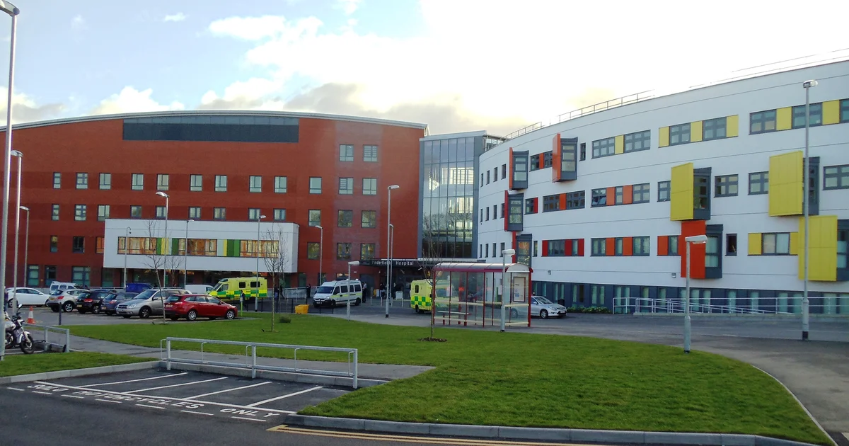 The main entrance to Pinderfields Hospital, Wakefield, with ambulances parked outside and the hospital's red-brick and white wings visible.